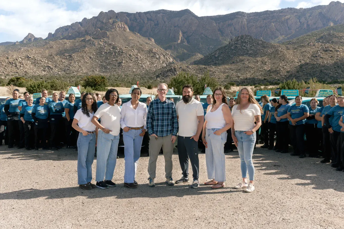 The Sandia Green Clean team and teal fleet gathered in front of the Sandia mountains in New Mexico